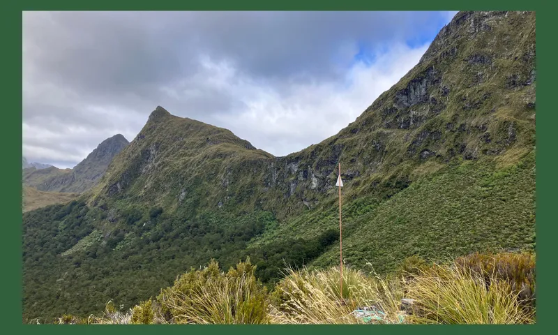 a dark green background with a little orange pole the only signs of human habitation visible with a dark steep and spiny ridge sidling into the sky