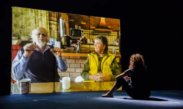 a projected video of a man and woman, with their daughter sitting in front of the screen