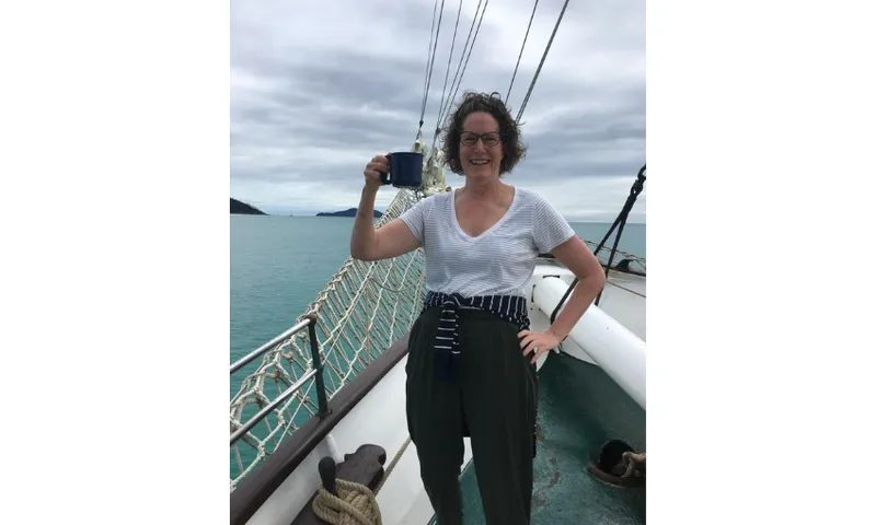 A photograph of Kate Camp on a yacht raising a mug in cheers.