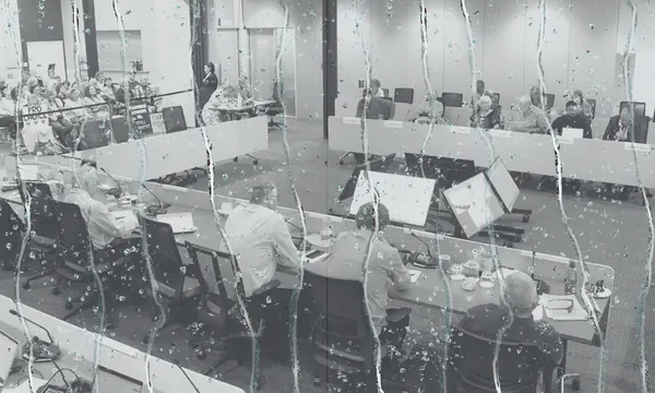 a meeting room filled with people seated at desks in a U shape. Dripping water is overlaid on top.