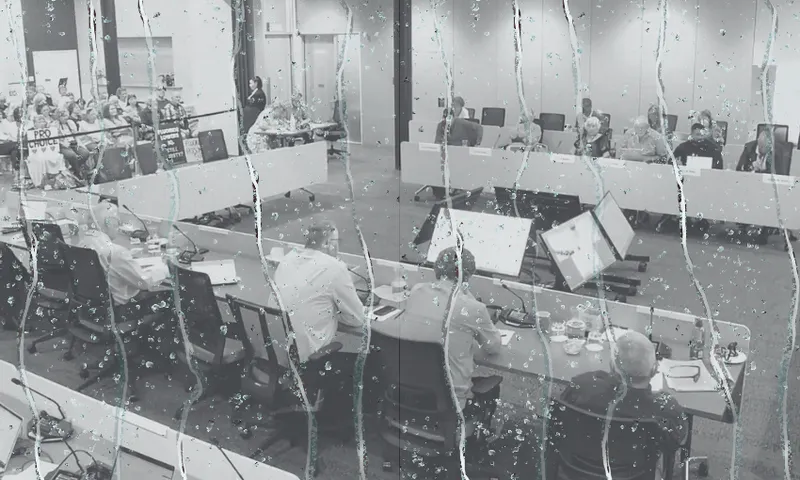 a meeting room filled with people seated at desks in a U shape. Dripping water is overlaid on top.