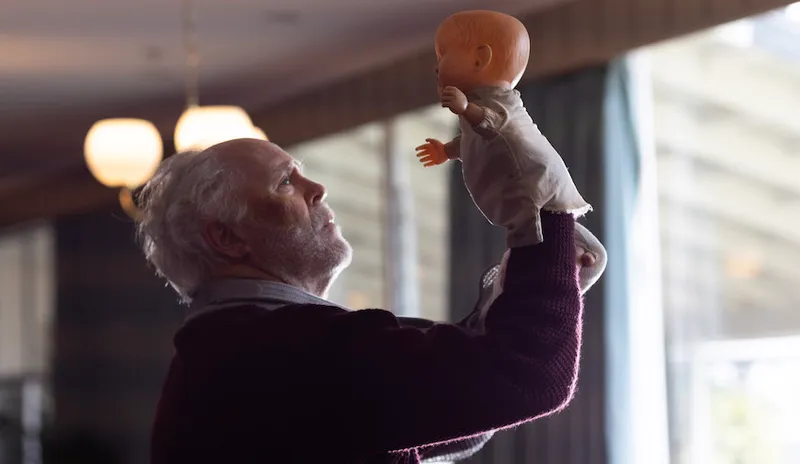 John Lithgow lifts up a doll puppet high into the air