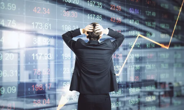 a man in a suit stands in front of a stock market board with his hands on his head in despair