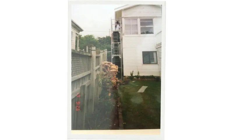 a portrait photo showing a tall scaffolding along the side of a house with people painting on it