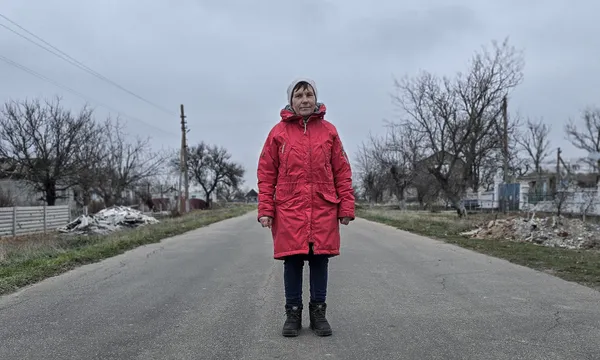 A woman wearing a red winter coat stands in the middle of a deserted road in Ukraine