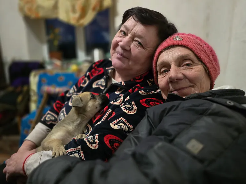 Two women hold a small puppy and wear warm clothing