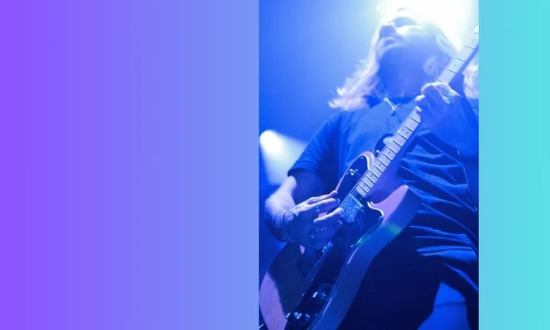 Dave Rowlands, the Fazerdaze guitarist with long hair plays an electric guitar on stage, illuminated by blue and purple lights. They wear a dark shirt, and a bright light shines behind their head. The background features a gradient of blue to purple.