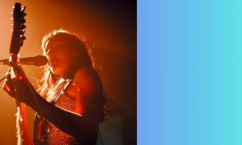 Amelia Murray Fazerdaze plays an electric guitar and sings into a microphone under warm orange stage lights. The background features a gradient from light blue to green.