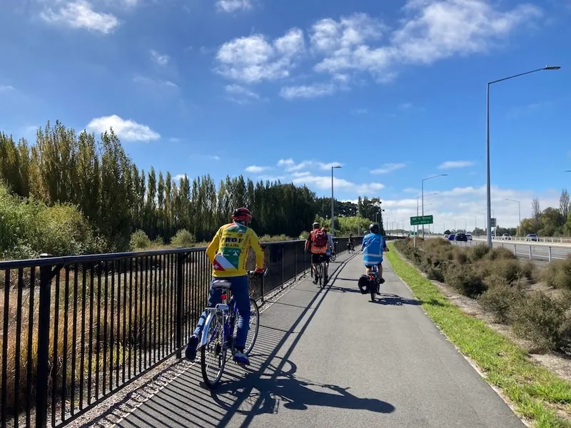 a blue sky and a group of people on a cycle lane next to a motorway
