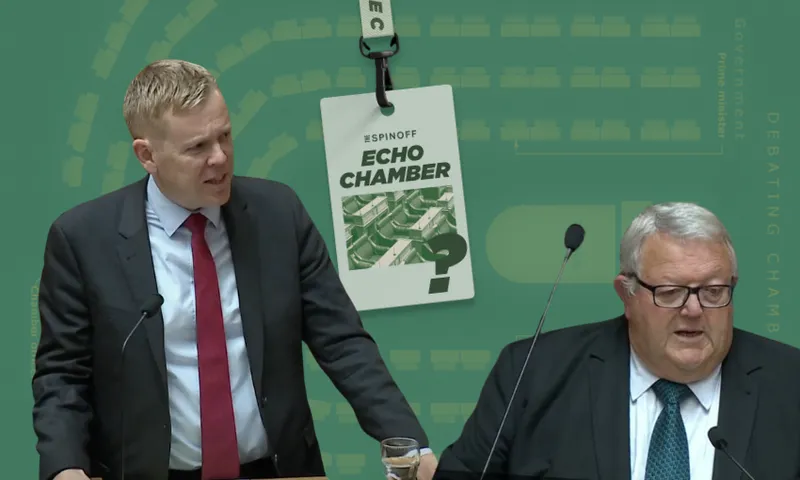 Two men in suits are speaking at podiums against a green background. One man is standing, gesturing with his right hand, the other is seated, reading. A conference badge with "Echo Chamber" hangs in the center of the image.