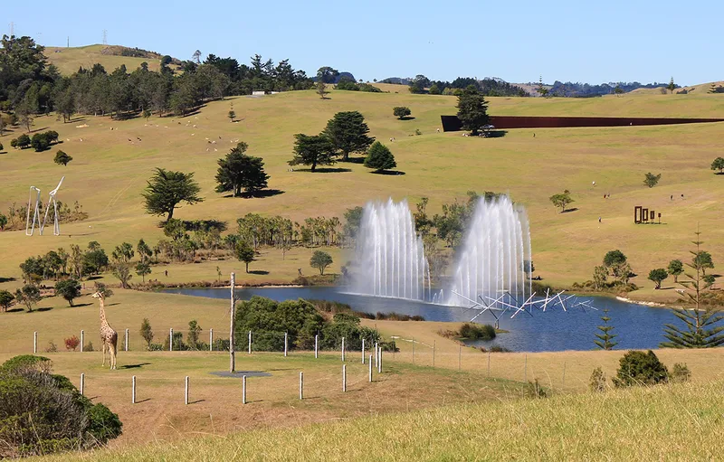 pastoral landscape with big artworks including a jet water fountain, a bit steel wall and a life-like sculpture of a giraffe