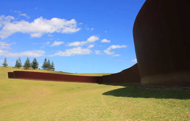 big curving rusty metal wall in a grassy field.