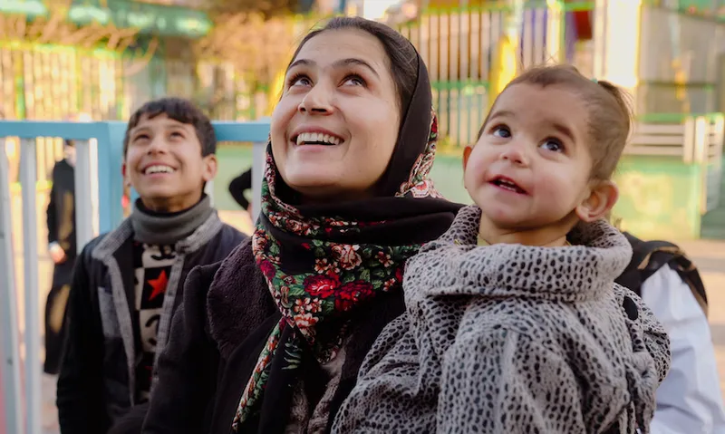A woman holding a young girl smiles and looks upwards at the sky