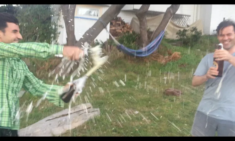 Photo of two people popping very fizzy bottles of beer in celebration.