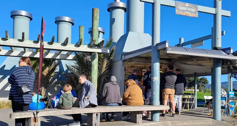 A photo of a quirky little building with lots of external beams. outside people are sitting on the bench and lining up at the window