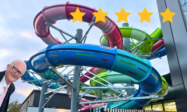 A man in a suit appears smiling near a colourful, winding water slide structure with multi-colored tubes. Five yellow stars are displayed above, suggesting a high rating.