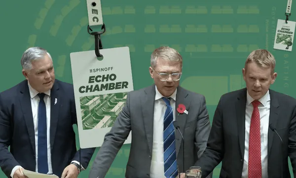 Three men in suits stand at podiums against a green backdrop with "Echo Chamber" written on it. They appear to be speaking or presenting, and one has a poppy on his lapel. A large ID tag with "The Spinoff Echo Chamber" hangs in the foreground.