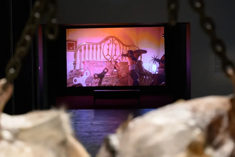photo of a projected film showing cowboy boots and a wrought iron bedframe