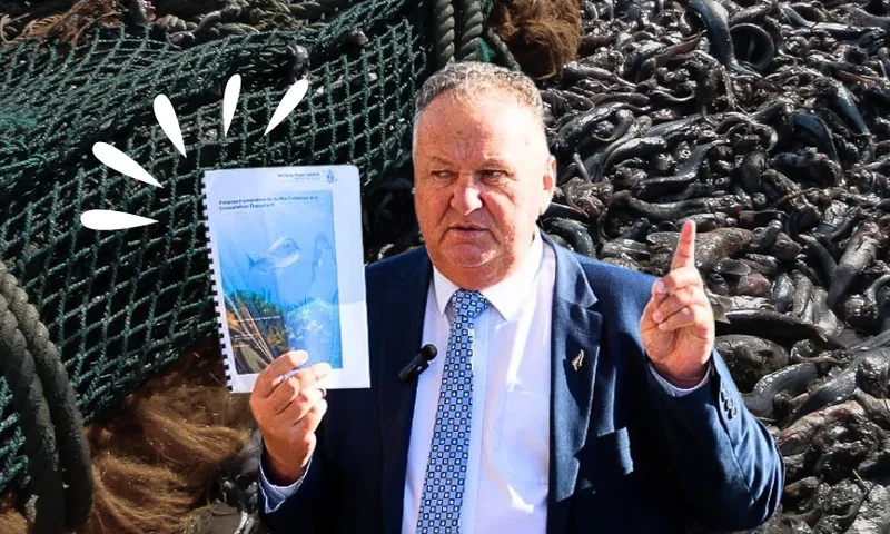 Shane Jones holding a printed document and pointing his finger. Dead fish and net behind him.