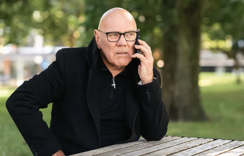 David Lomas sits on a park bench while taking a phone call