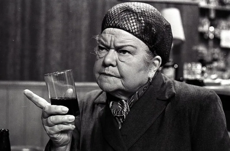 A black and white image of an woman in a hairnet, frowning and pointing