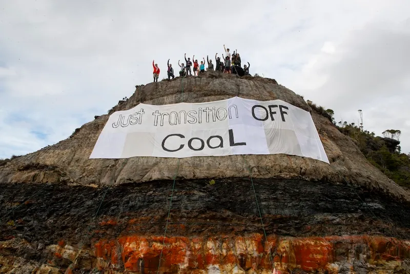 a group of people on top of a hill with a large banner hanging down over the exposed earth saying 'just transition off coal"