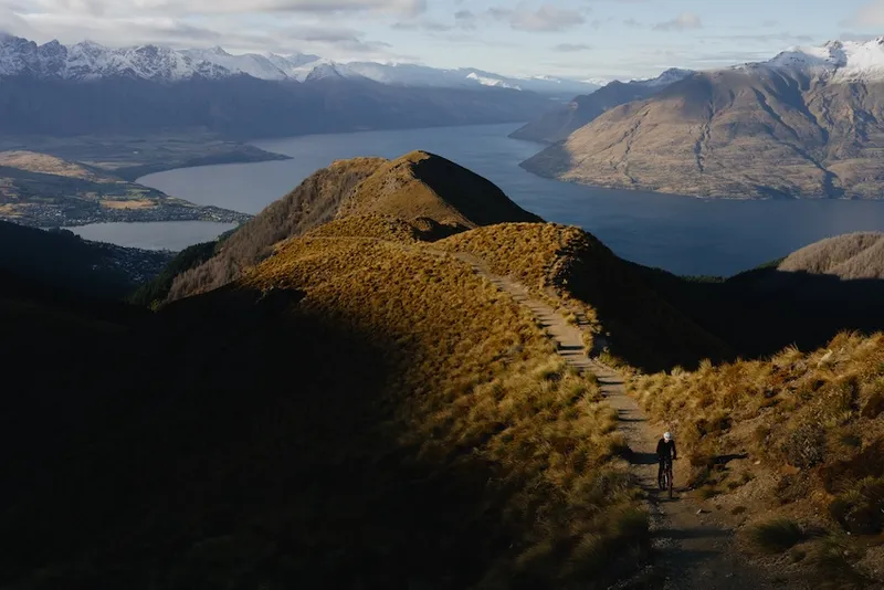 golden light illuminating the tussocky upland of the benlomond ridge, with Benhildred a small dot making his way uphill, Lake Wakatipu dark and blue far below
