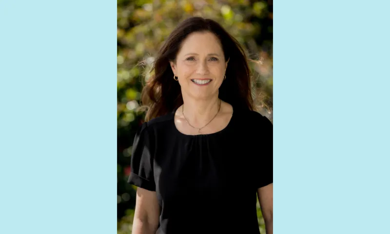 a photo of a smiling white woman wearing a black tshirt against a background of trees