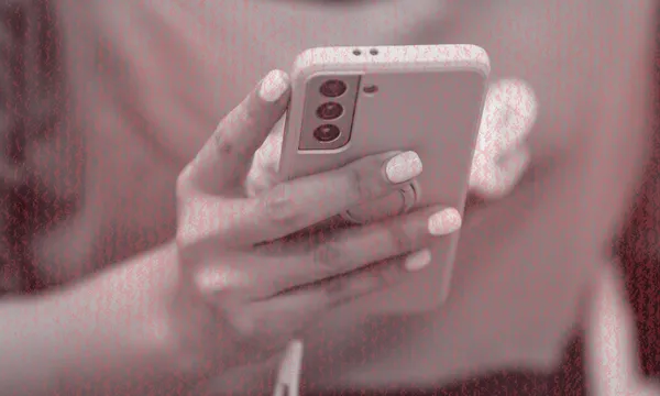 A person holding a smartphone with a white case, using their thumb to interact with the screen. The image has a red filter and shows only their hands and part of their torso.