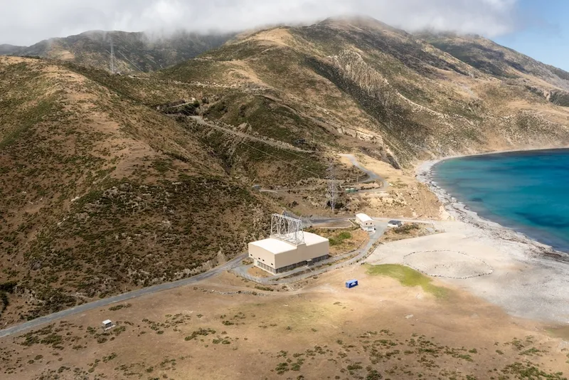 brown scrubby hills and a little white substation next to a turquoise curve of water