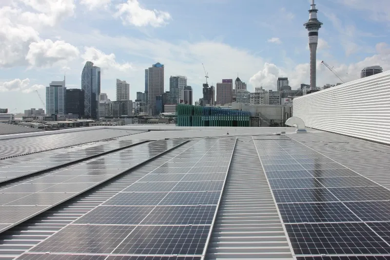 solar panels on the roof of a building with Auckland's skyline of high rises, including the Sky Tower in the background