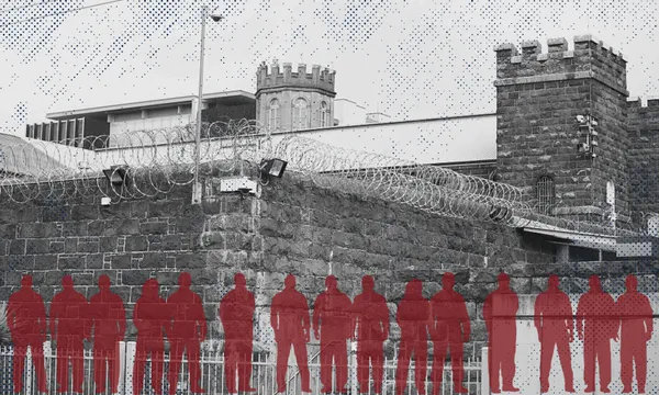 A stone prison wall topped with barbed wire stands in front of castle-like towers; a row of red silhouettes of people is overlaid in the foreground.