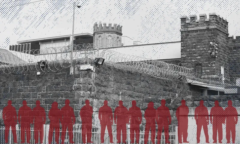 A stone prison wall topped with barbed wire stands in front of castle-like towers; a row of red silhouettes of people is overlaid in the foreground.