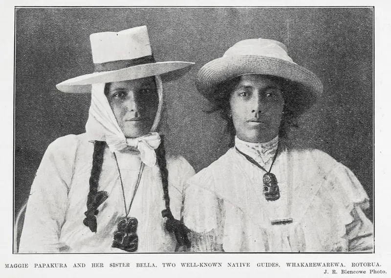 Two Māori women in white dresses and wide-brimmed hats, both wearing pounamu pendants. The photograph is black and white and captioned as Maggie Papakura and her sister Bella, guides from Rotorua.