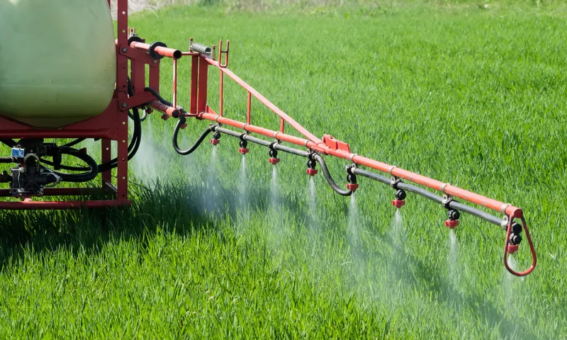 a red machine with lots of nozzles spraying a fine whit substance onto a verdant field