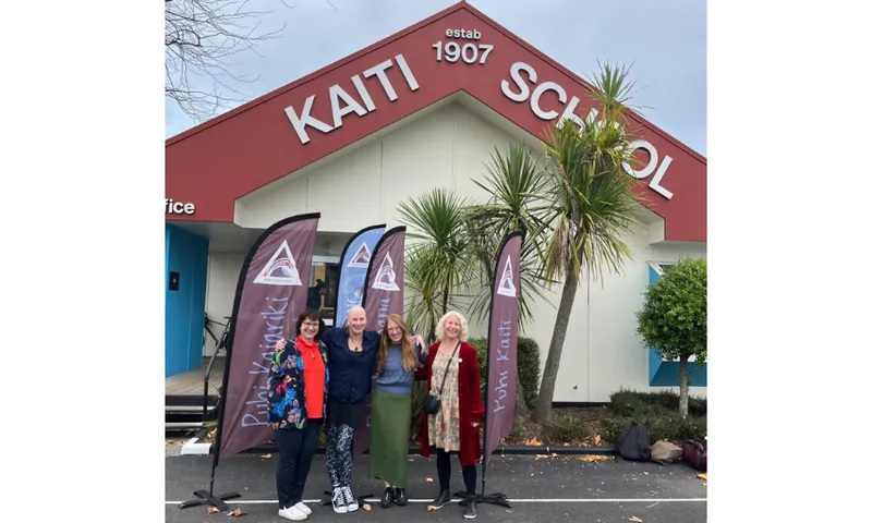 Photo of four women standing in front of a school building with the words Kaiti School painted on the roof facade.