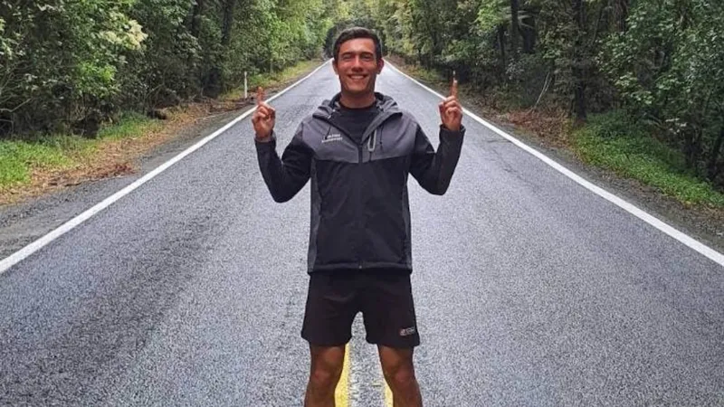A man stands in the middle of a road with his hands up, smiling