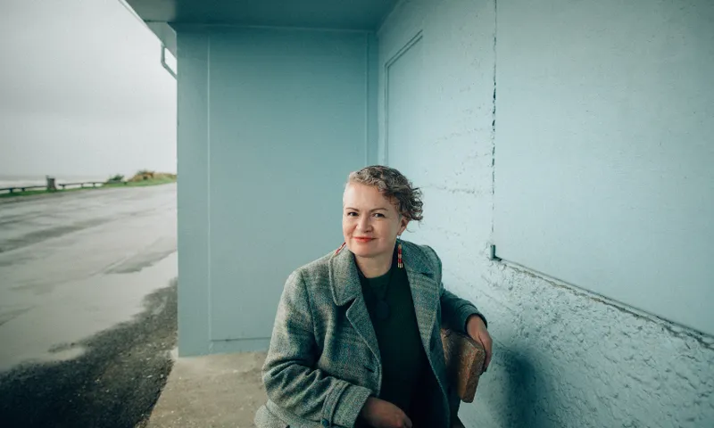 A photograph of a woman, smiling in an outdoor setting with pale green background.
