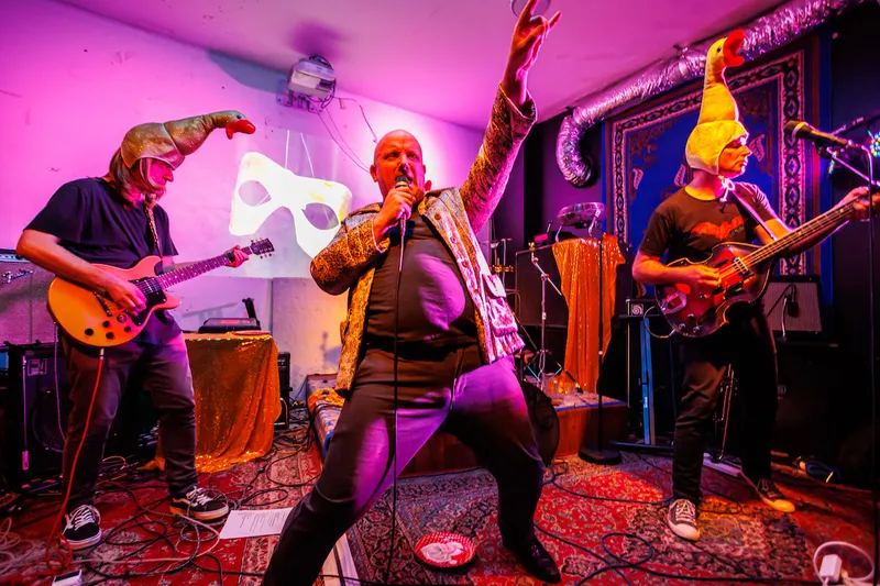 Thee Golden Geese performing in pink lights with funny hats on