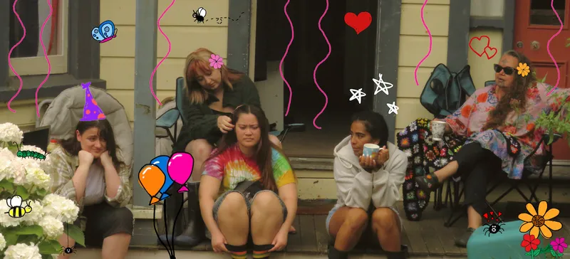 young adult girls on the front porch of a house, one drinking a cup of tea another braiding hair