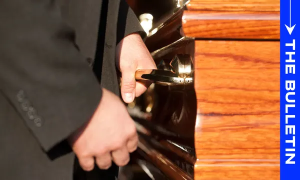 Male hands hold the handles of a funeral casket