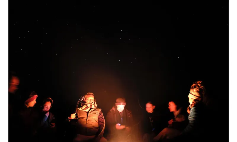 People huddled around a fire with the night sky showing stars above them.