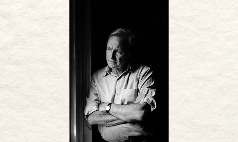 A man is standing leaning against a wall, looking off to the right. He has his arms crossed. The photo is in black and white.