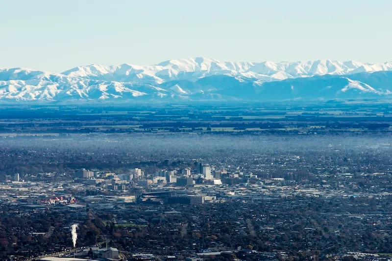 the city of chrsitchurch with sparkly alpine mountains in the background and and a miasma of fog poised over the centre city