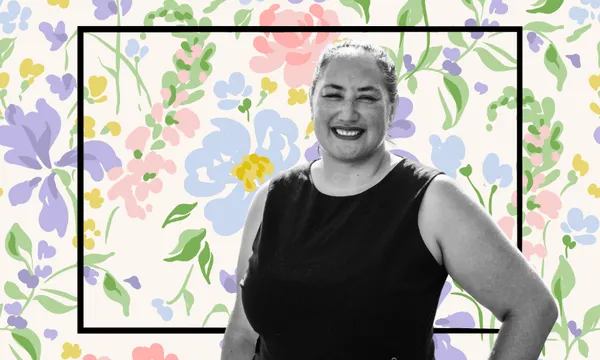 A woman smiling in a sleeveless dark dress stands in front of a colourful, floral-patterned background with a rectangular black border framing her.
