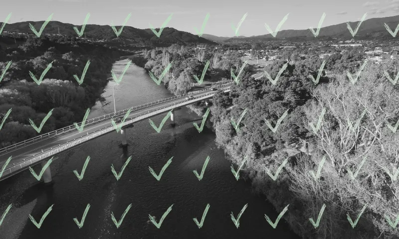A black and white aerial view of a river and bridge surrounded by trees, with a grid of translucent green check marks overlaying the entire image.