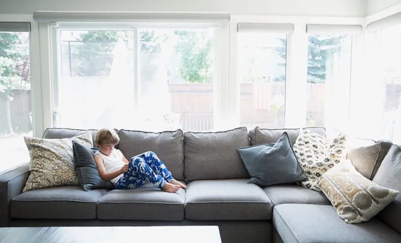 Boy in pajamas using digital tablet on living room sofa