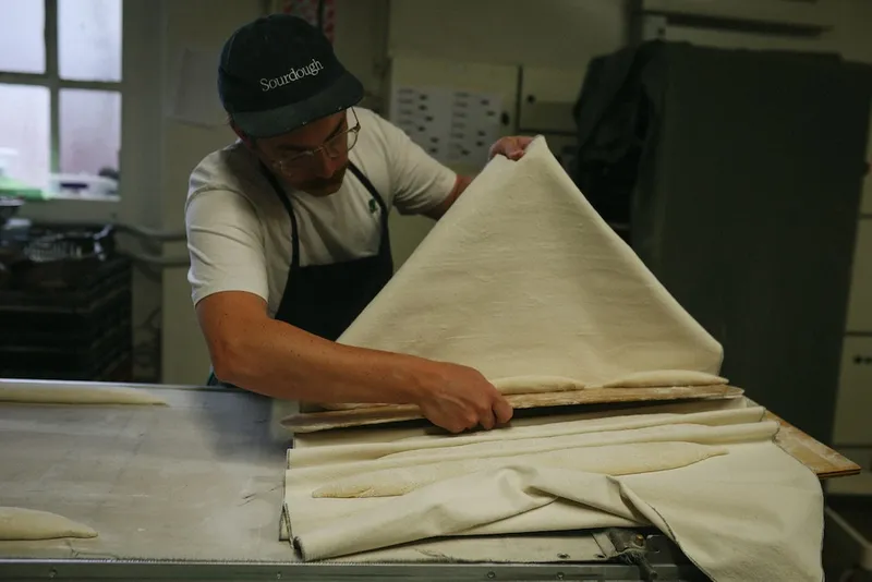a baker in an artfully lit shot slides some uncooked baguette onto a tray