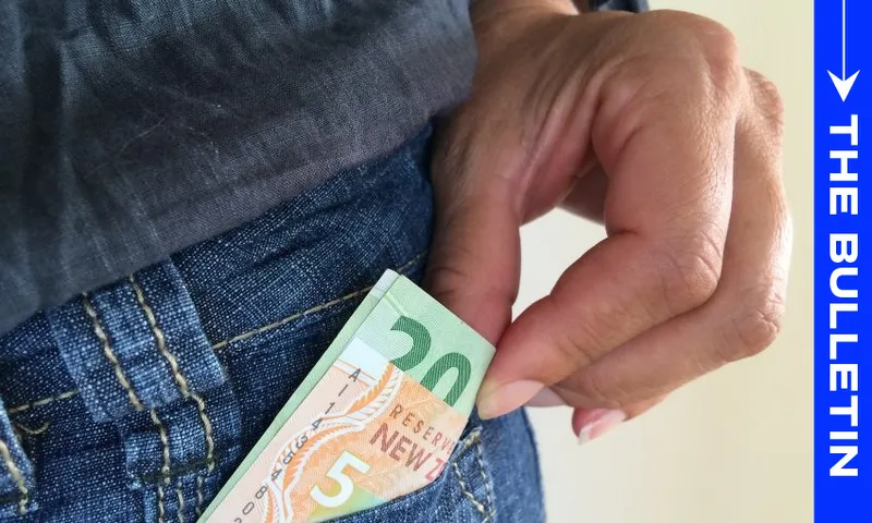 A hand places a New Zealand 20 dollar banknote into the front pocket of blue jeans. A vertical blue banner on the right side reads "The Bulletin.