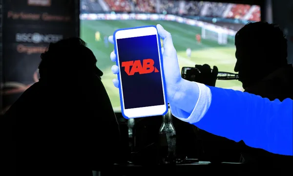 a picture of people watching TV with a hand holding a phone with a TAB logo on it